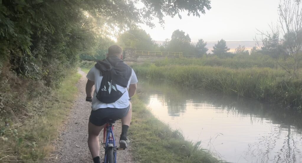 Rear view of a man cycling next to a canal in the evening just before dusk. 